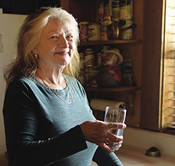 woman standing by kitchen sink, holding a glass of water