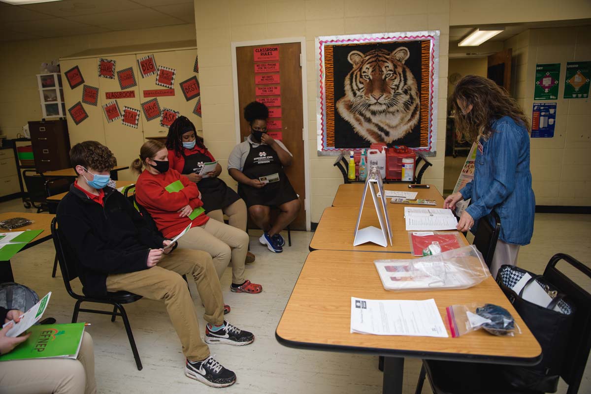 Four students listen as a woman lectures the class.