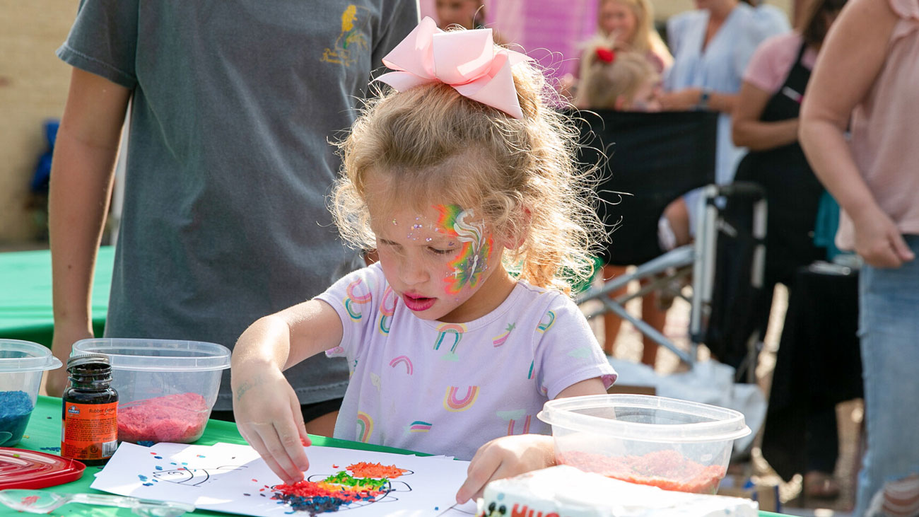 A girl creating a picture with painted rice.