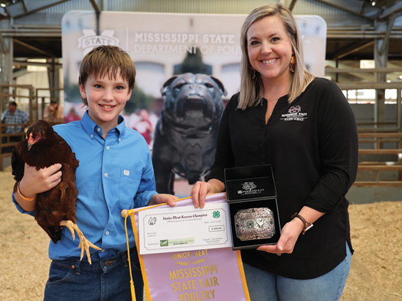 A young boy in a blue shirt proudly holds his award-winning bird while accepting his prize.