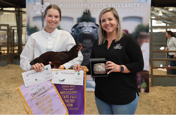 A young girl in a white shirt holds her award-winning bird while accepting her prize.