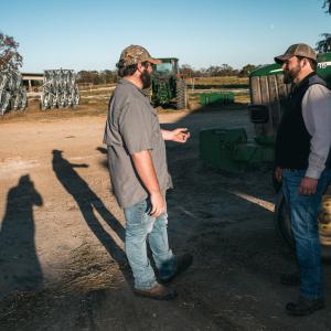 A standing man gesturing toward another standing man.