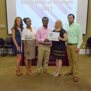 A teen wearing a pink shirt accepts a certificate from a group of three women and one man.