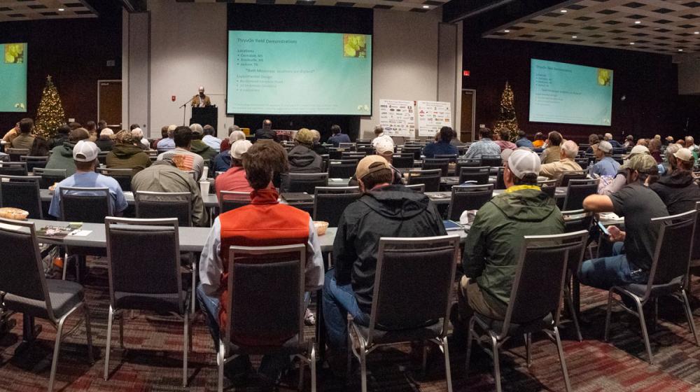 A panoramic image of a large crowd of people with two large screens in the back.