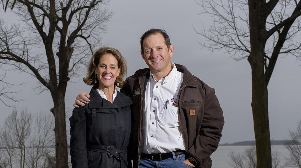 Row Crop Producers John and Nancy McKee A man stands next to a woman with his arm around her shoulders while they both smile at the camera; a lake rests in the background.