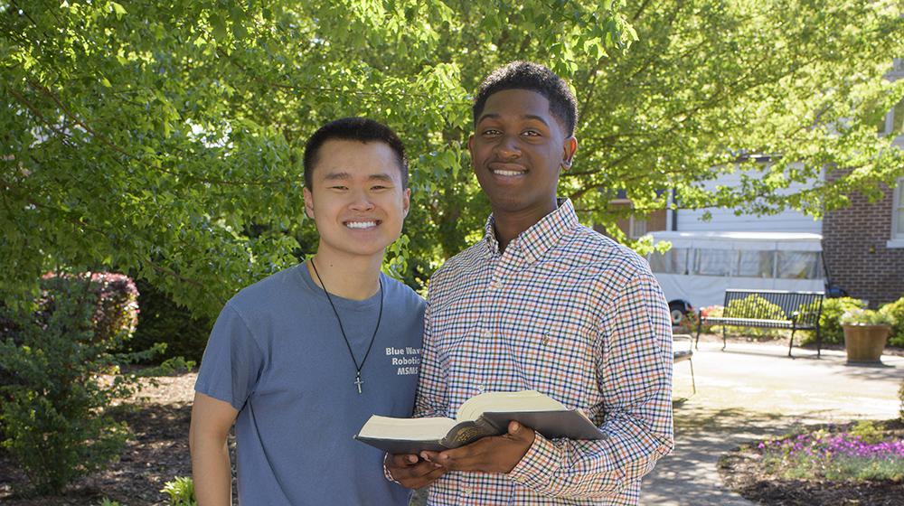 Holmes County 4-H’er Tyler Branch (right) with classmate Devin Chen. A boy wearing an orange and blue plaid shirt and holding an open book stands next to another boy wearing a blue shirt. Photo credit: Kevin Hudson
