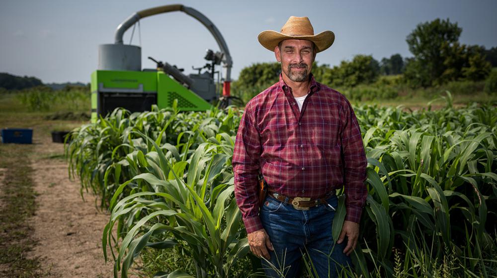 A man wearing a large hat and red shirt standing in a field.