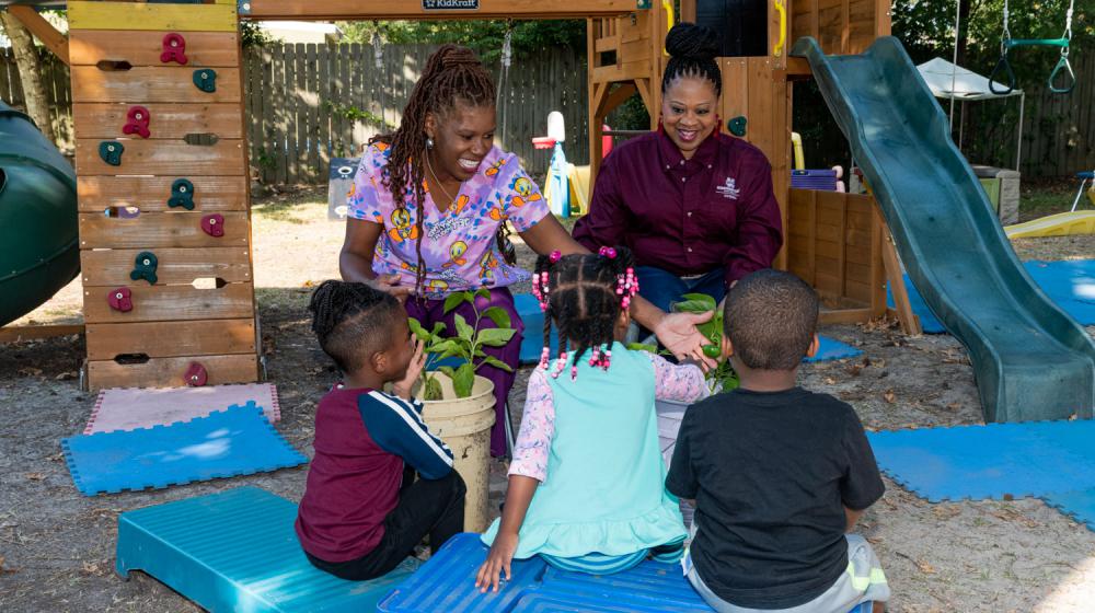 Two adults, smiling, working with three small children.