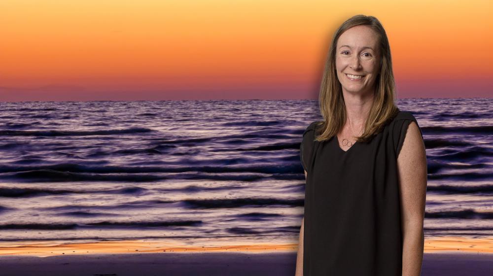 A woman, smiling, standing in front of the ocean