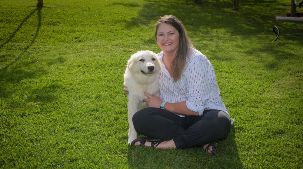A woman, smiling, sitting with her arms around a large dog.
