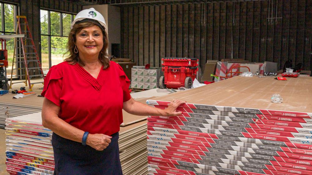 A woman wearing a hard hat standing beside a stack of pallets.