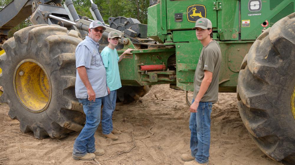Three men standing in front of a piece of logging equipment.