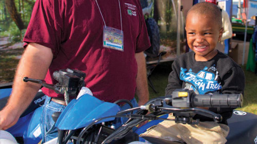 A man stands next to an ATV with a young boy sitting on the seat.