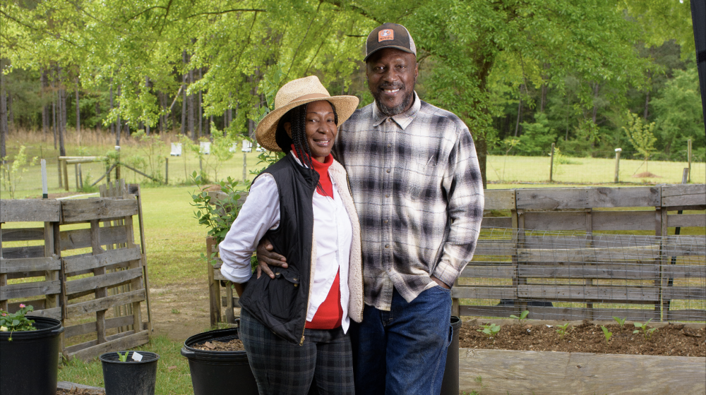 A smiling couple standing next to each other in a garden.