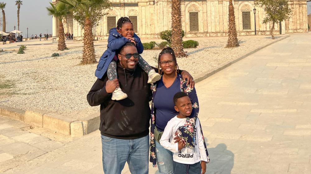 A Black man and woman standing with a boy and a girl in front of a mosque in the desert.