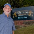 A man stands in front of a sign that reads, “Saltillo Mississippi, Welcome Home.”