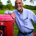 Smiling man in gingham dress shirt leans on a tractor