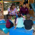 Two adults, smiling, working with three small children.