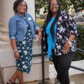 Two women standing in front of a column, smiling.