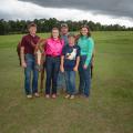 Five people smiling with three horses, all standing on a grassy plain