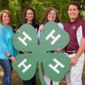 Three women and one man hold a large 4-H clover