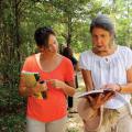 Two women walk and look at a book.