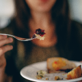 A person holding a fork and plate with food on it. 