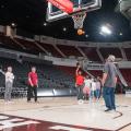 One man shoots a basketball on a court as others stand nearby.