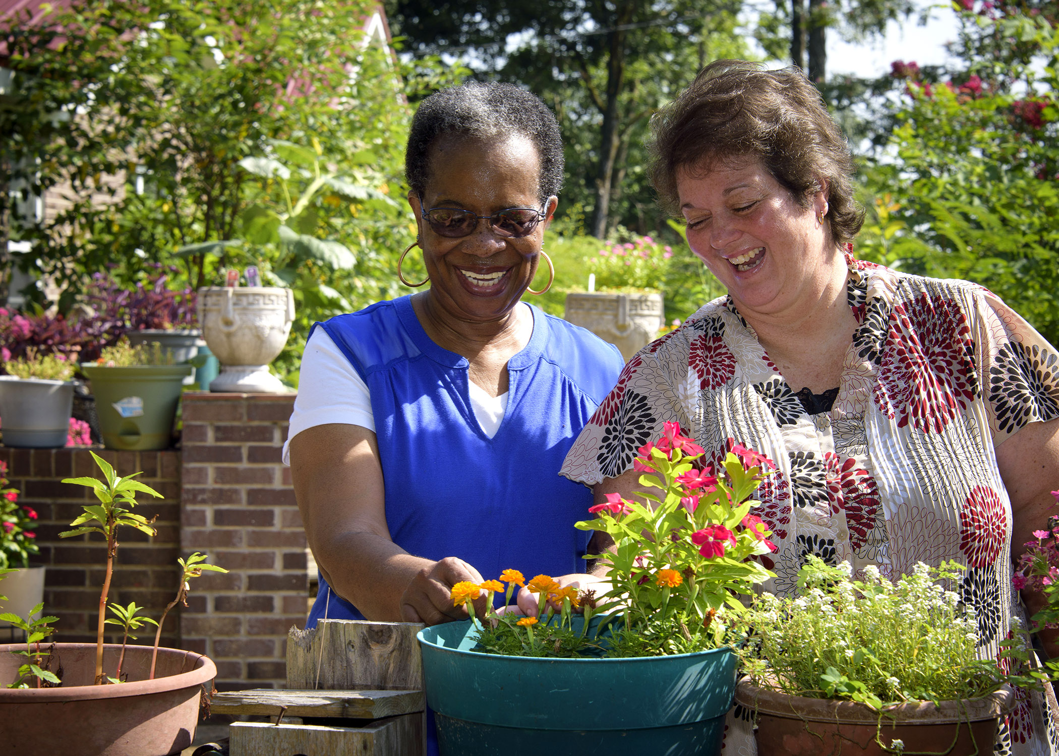 Two women smile as they enjoy colorful potted ornamental plants.