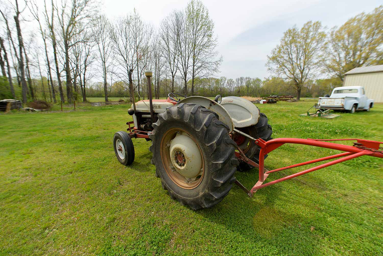 An orange tiller with black wheels faces a treeline.