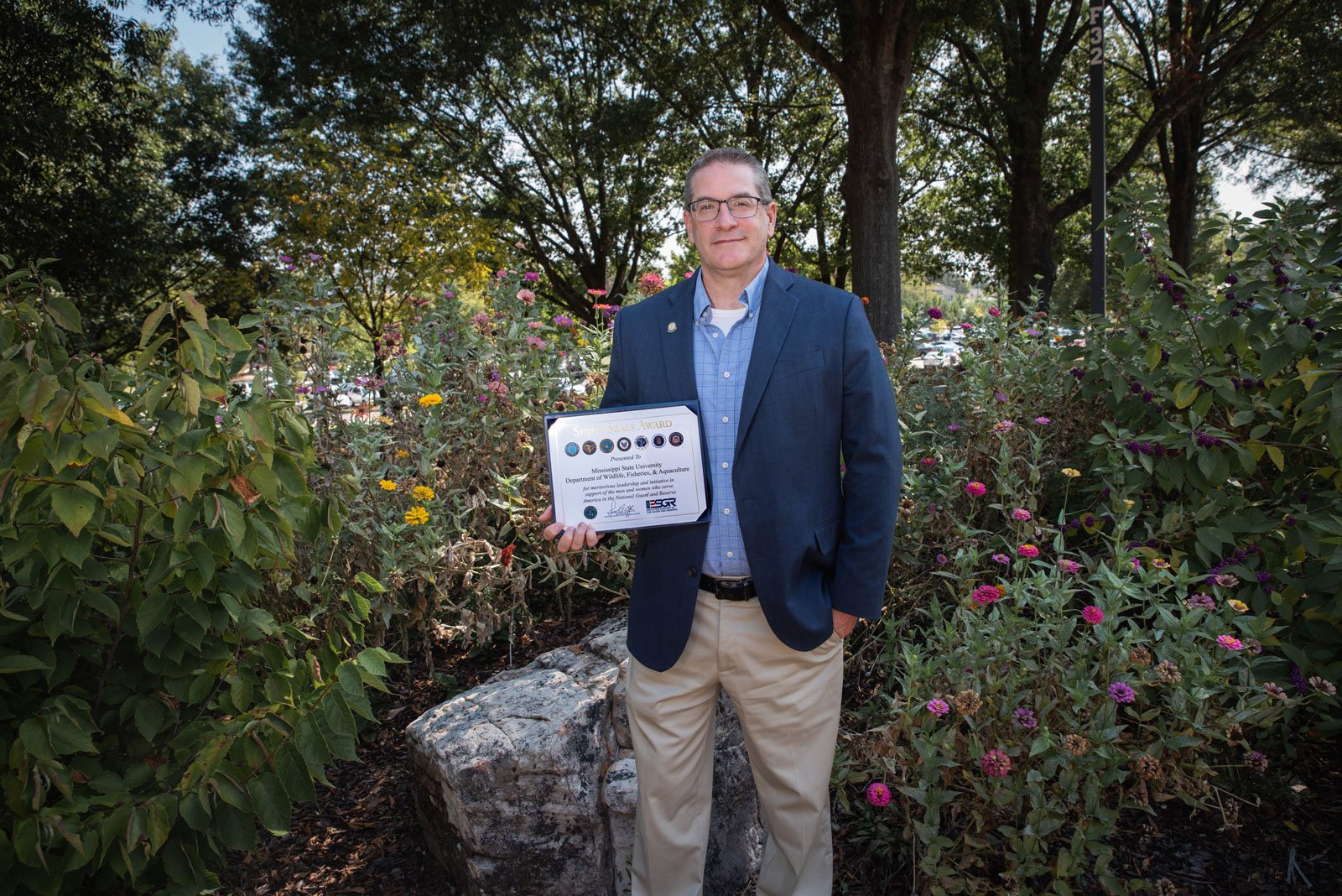 A man standing with a plaque that lists “Seven Seals Award” on it.