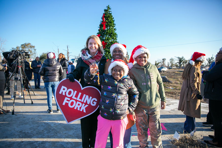 Two women with a boy and a girl, all smiling and standing in front of a Christmas tree.