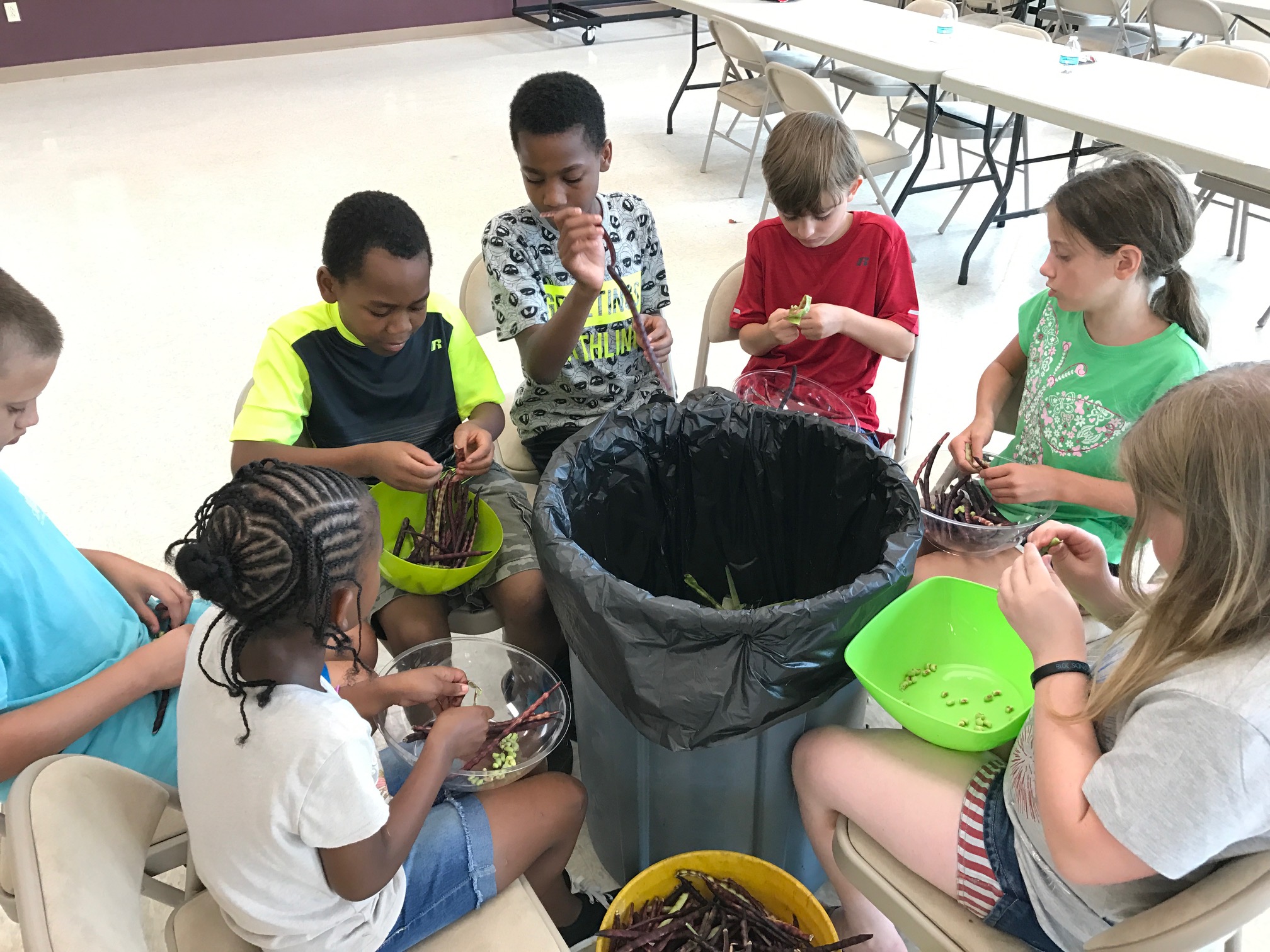 Children sit in a circle as they shell peas.