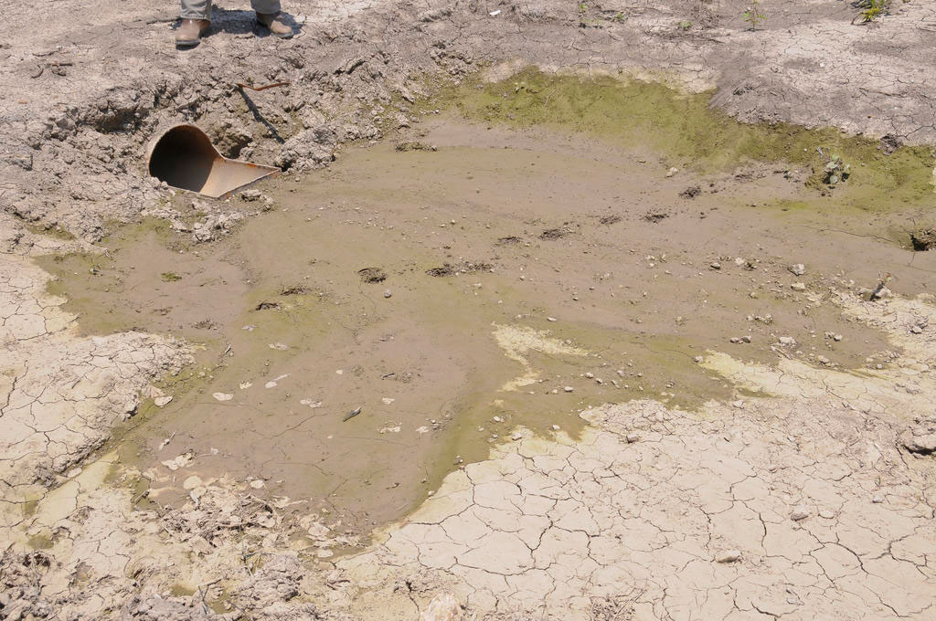 A large pipe coming out of the ground, which is muddy right at the pipe's opening and dry farther away.