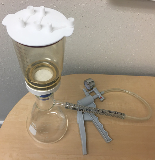 The full apparatus of vacuum pump, flask, bottle, tubing, and funnel is assembeled on a table.