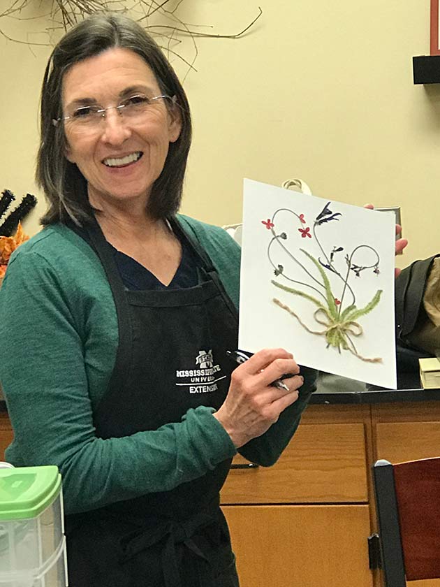 A person holds up a paper with a flower arrangement example.