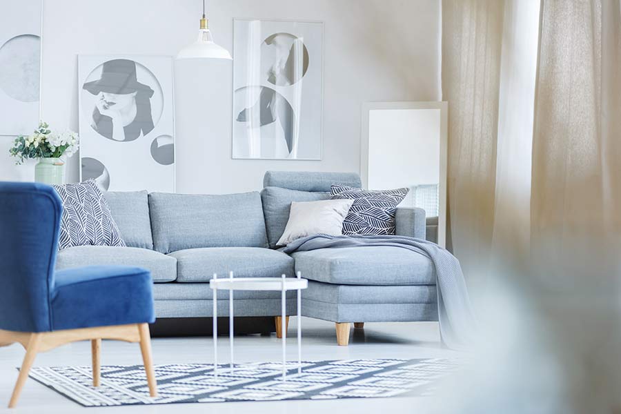 A living room with white and off-white walls and curtains. The furniture and carpet are various shades of blue. 