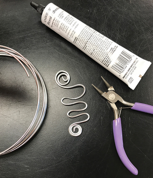 Jewelry pliers, wire curled into a wave shape with curlicues on each end, and a tube of glue.