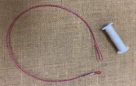 Pink floral wire bent into large, opened loop displayed on burlap cloth next to spool of thread.