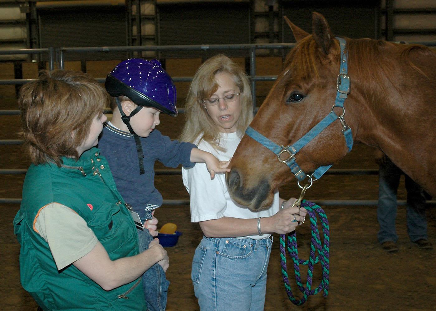 Oktibbeha County Hospital physical therapist Glenda Tranum holds Preston Cook, age 3, up to pet his therapy horse before a recent hippotherapy session at the Mississippi Horse Park. Denise Latil helped handle the horse throughout the session. The Mississippi State Extension Service 4-H TEAM (Therapeutic Equine Activity Member) Program is one of two accredited therapeutic riding programs in the state.