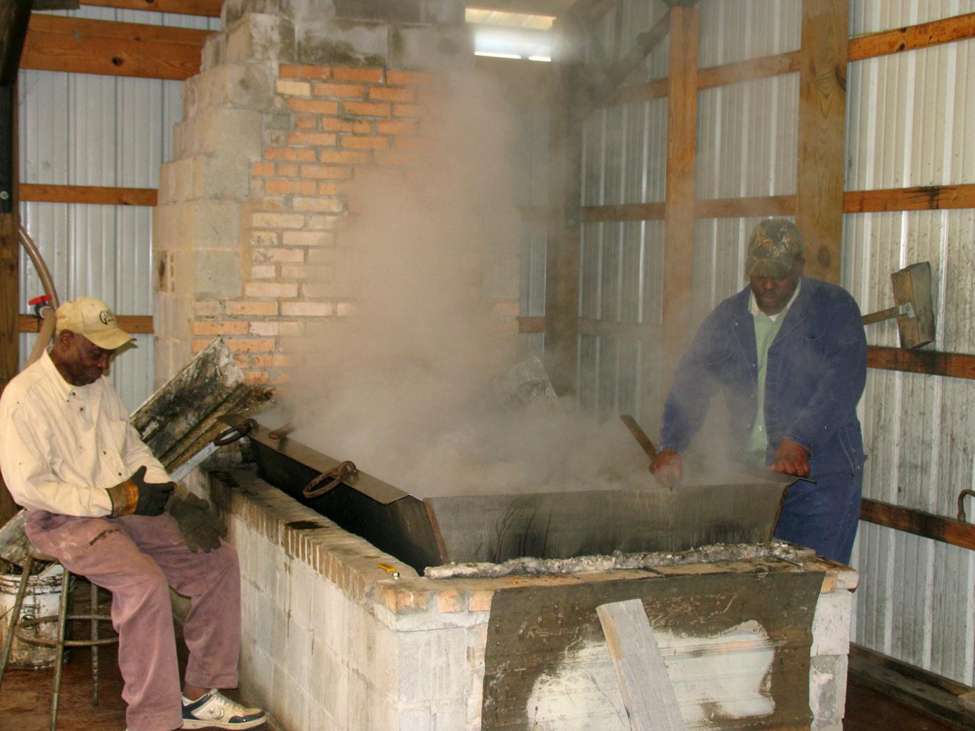 Hosea Brown, right, cooks down sugar cane syrup to molasses the old-fashioned way over a wood fire in his family business in Jefferson Davis County. Family friend Joe Norwood helps with the work at My Paw Paw's Ole Fashion Molasses in New Hebron. (Photo by Prentiss Headlight/Shirley Burnham)