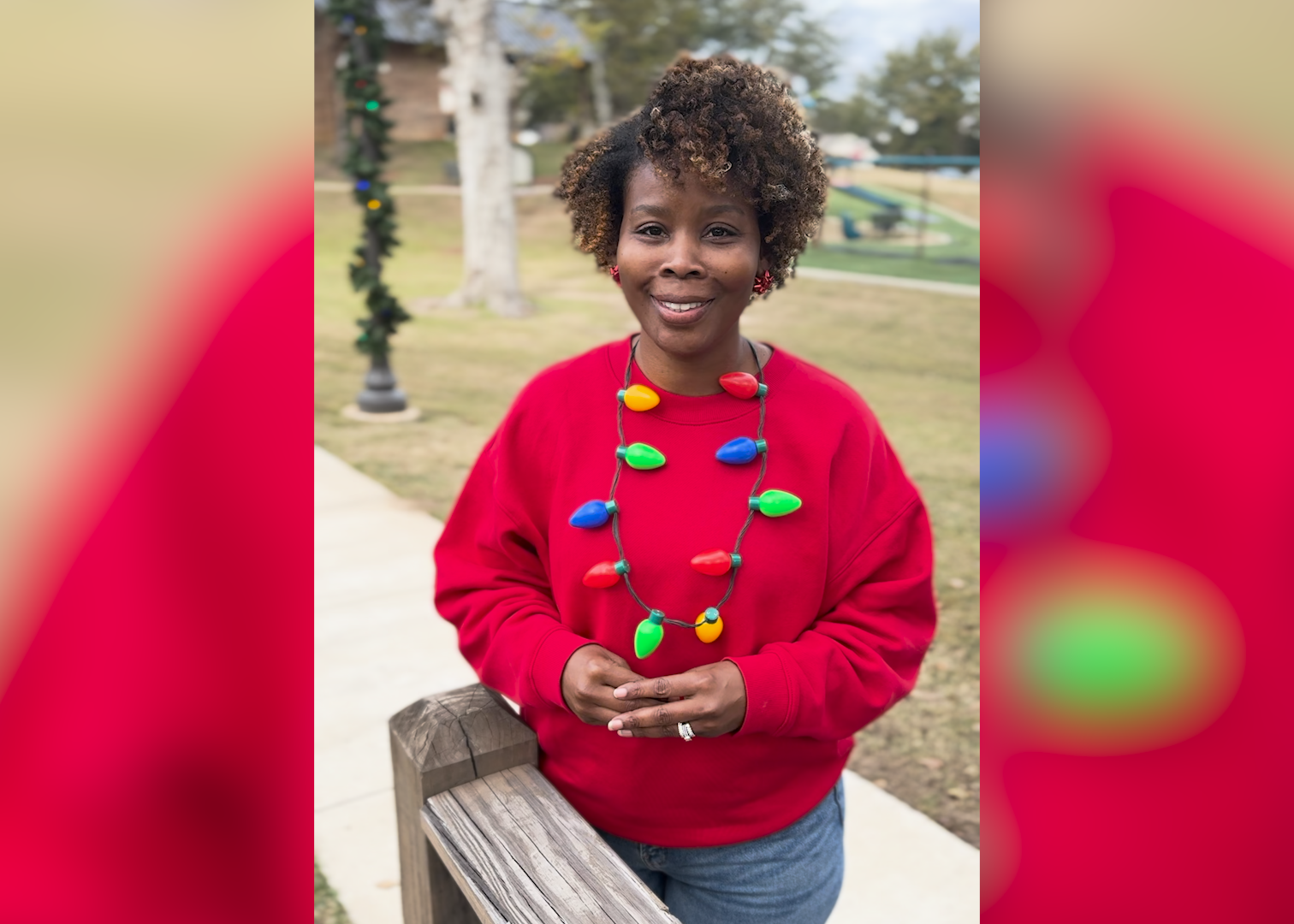 A woman stands on a sidewalk in a red sweatshirt and festive holiday-themed necklace.