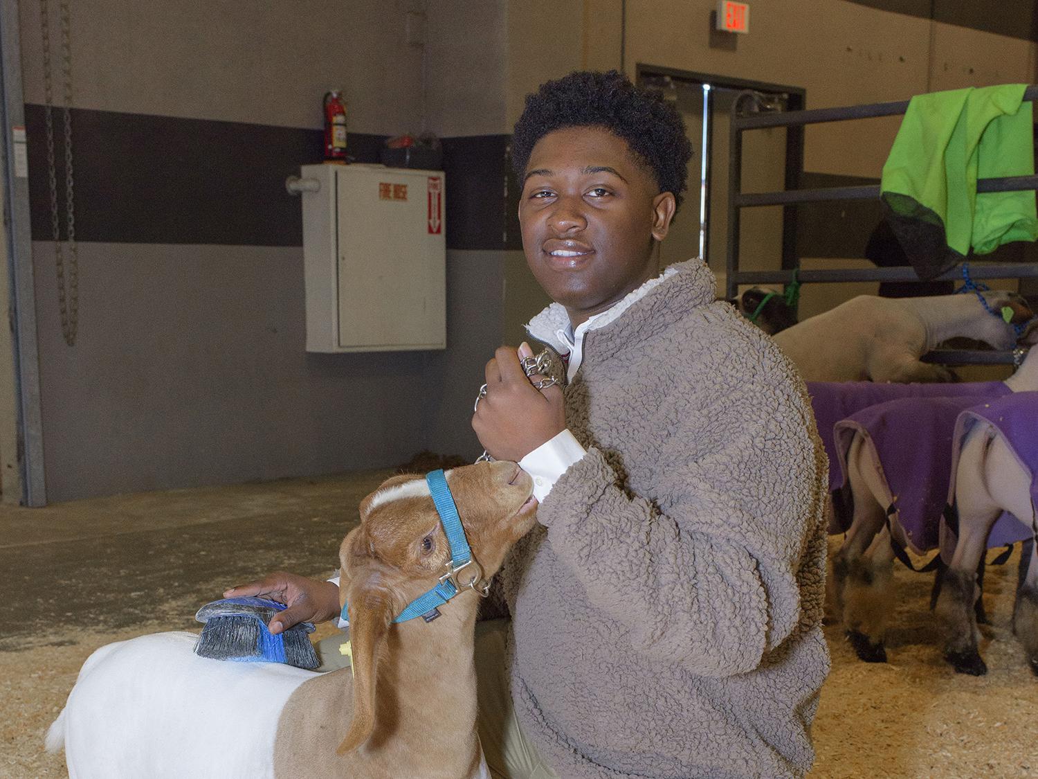 A young man kneels next to his goat at the Dixie National Sale of Junior Champions.