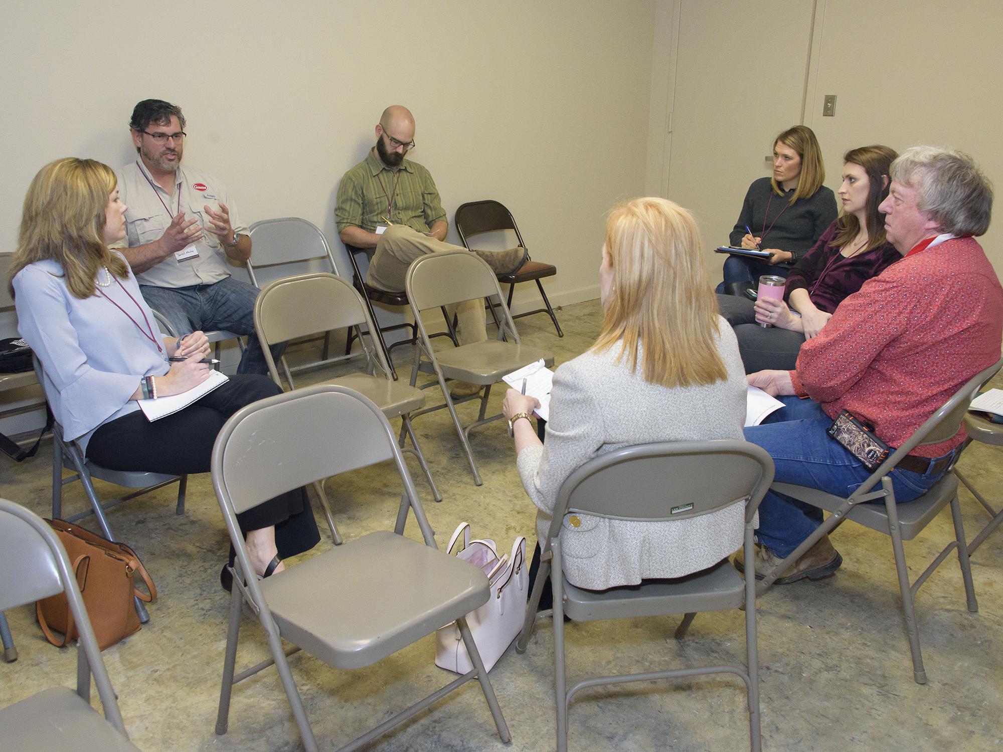 Man in glasses speaking to a group of people sitting in a circle.