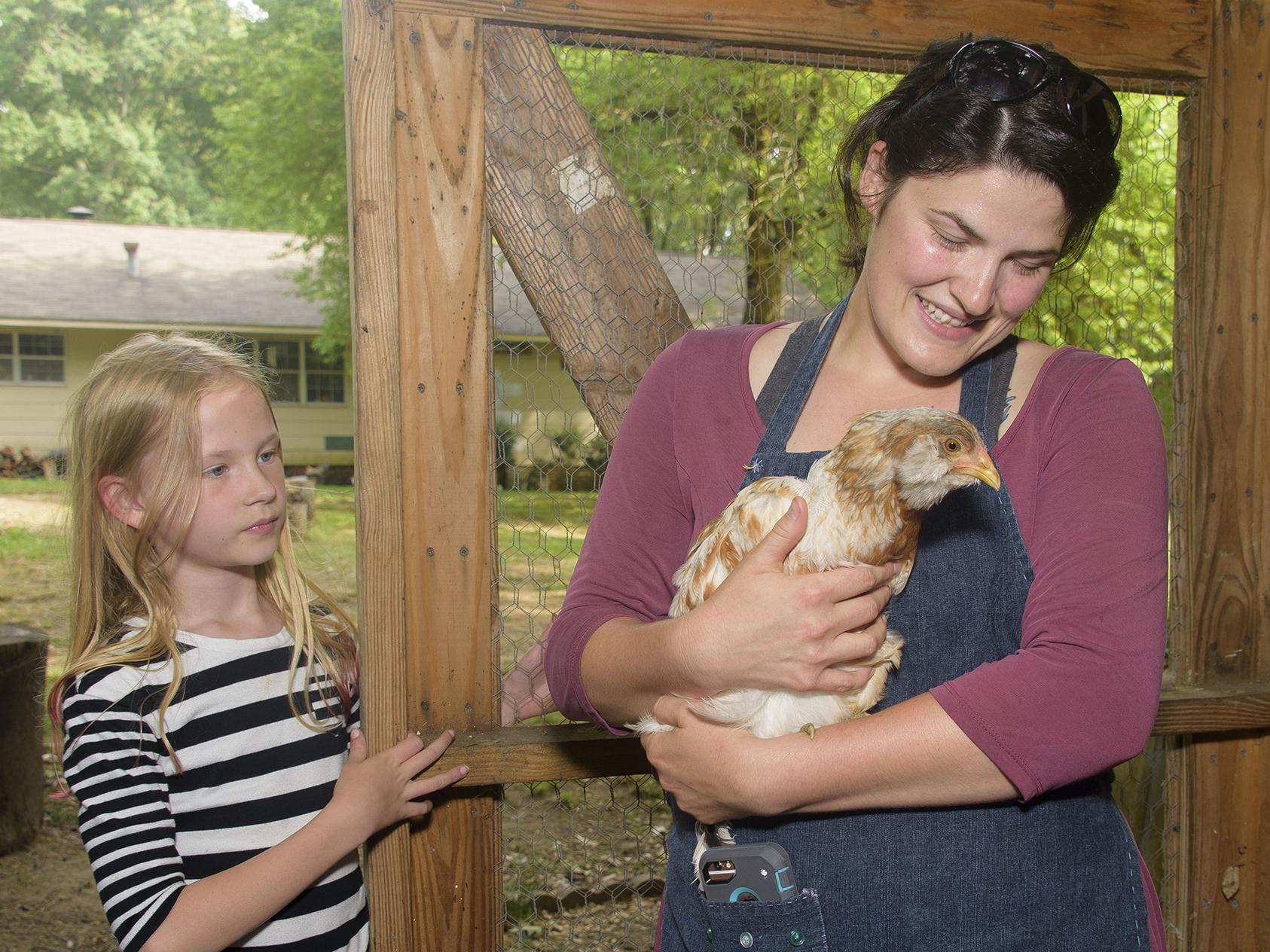 A woman holds a brown and white chicken while a young girl looks on.