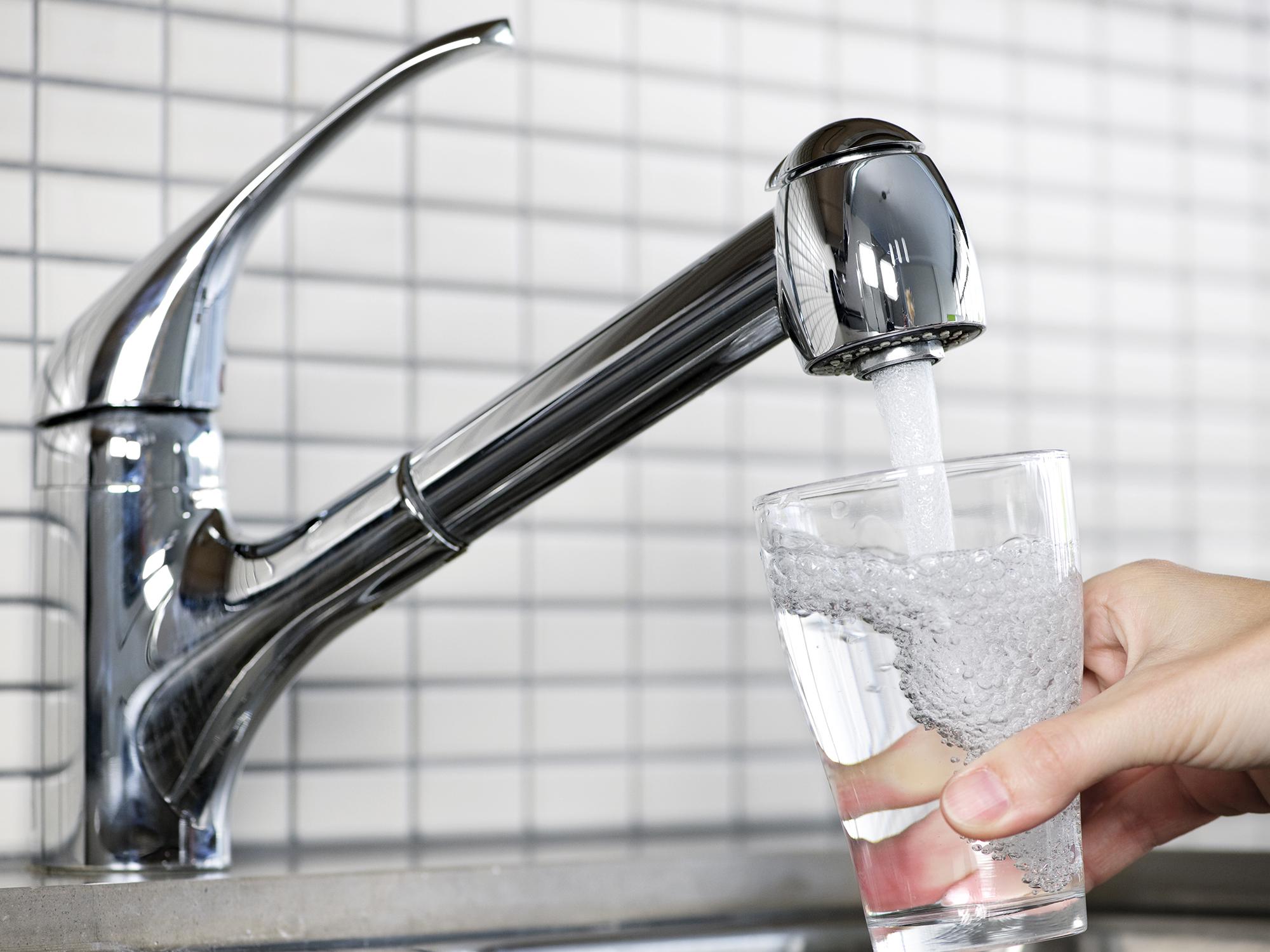 Water flows from a stainless steel kitchen faucet into a clear drinking glass.