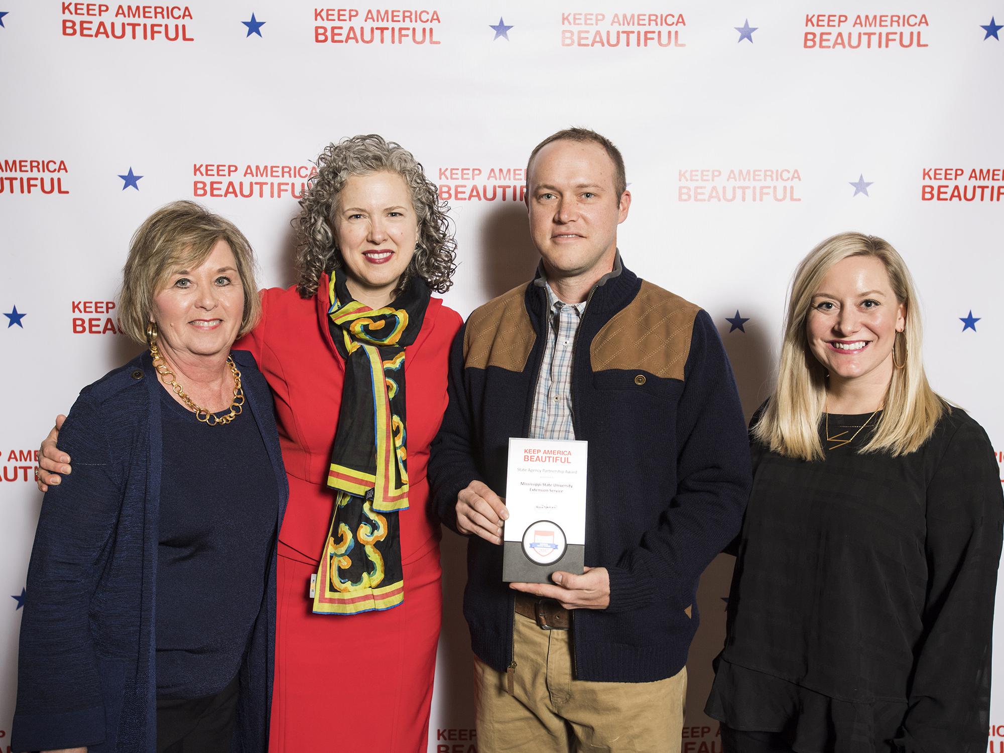 Four people pose for a photo with the award presented to the Mississippi State University Extension Service for its support of the Wildflower Trails of Mississippi Project.