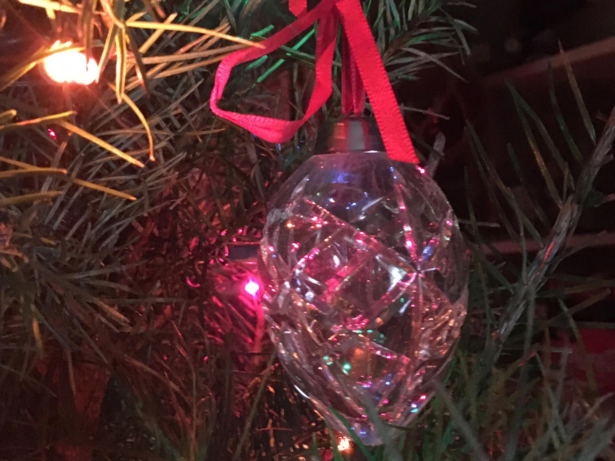 A small pink stocking with a white fuzzy top hangs from a Christmas tree inside a house.