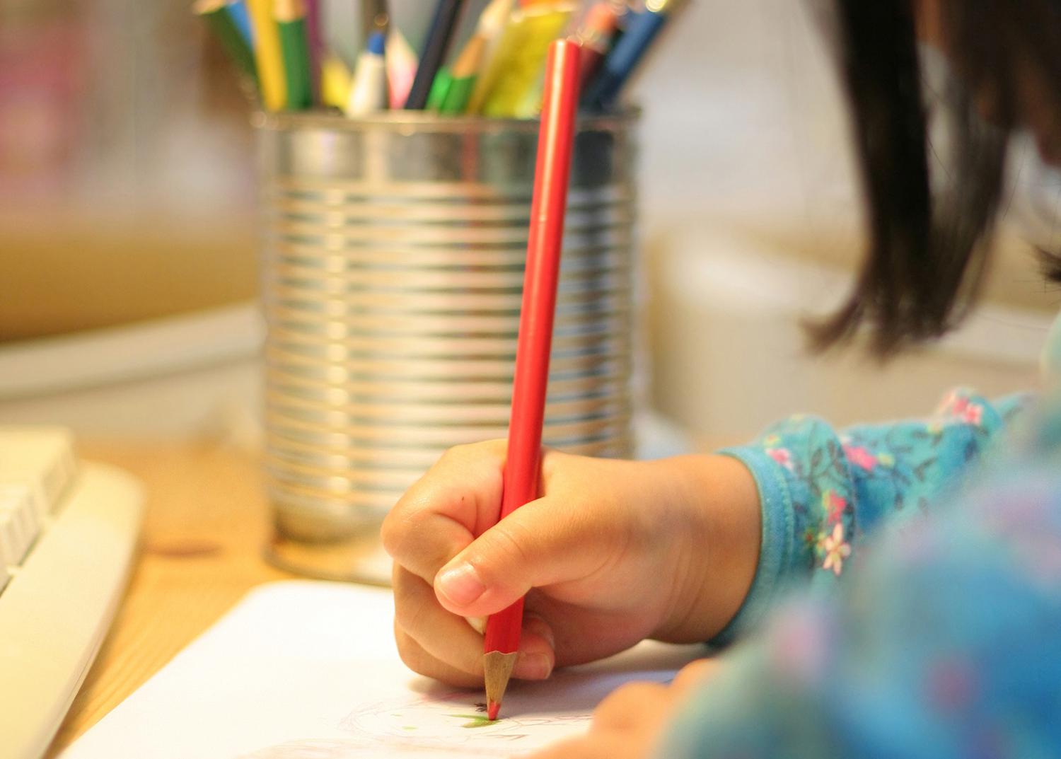 A child uses a colored pencil to write on a sheet of paper.