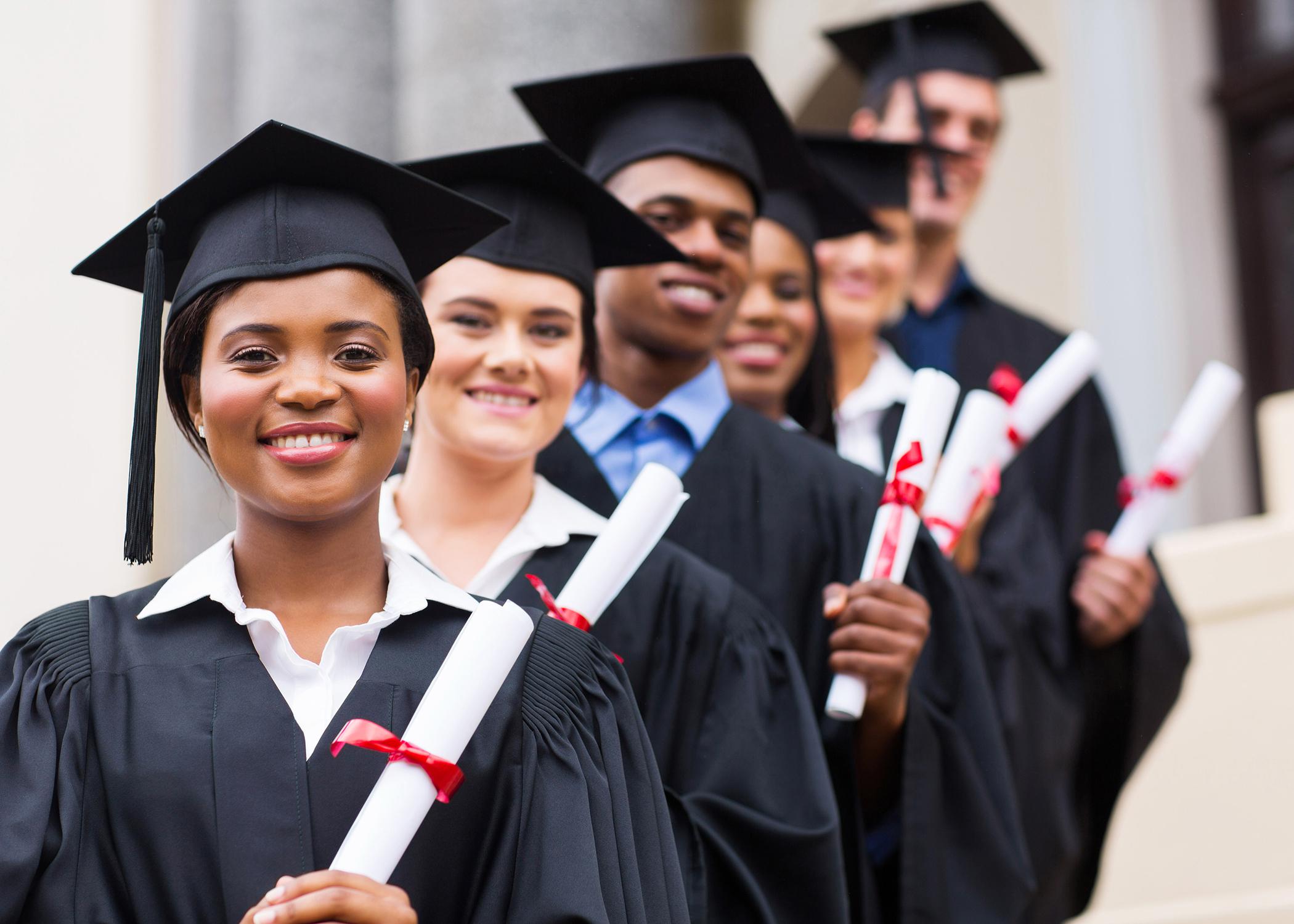 A group of smiling graduates pose in caps and gowns.